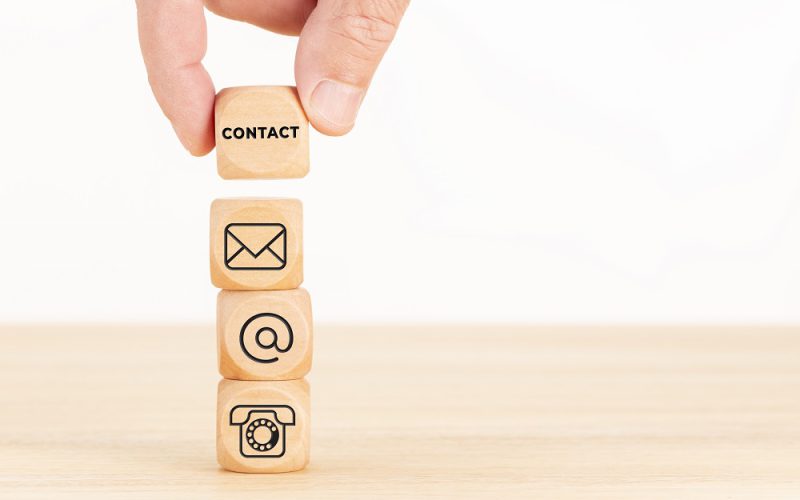 Contact us concept. Hand holding a wooden block with text and a pile of dices with communication icon. Copy space